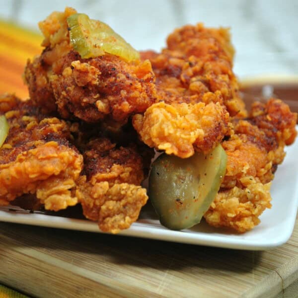 Nashville Chicken with Pickles on a white plate on a wood cutting board