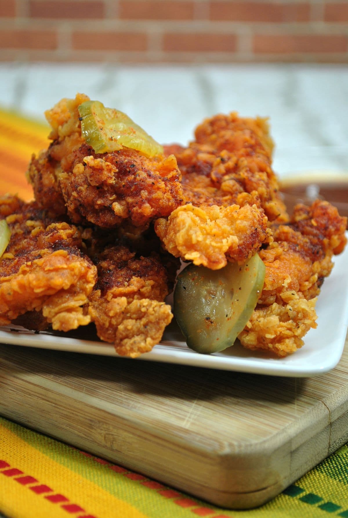 Nashville Chicken with Pickles on a white plate on a wood cutting board