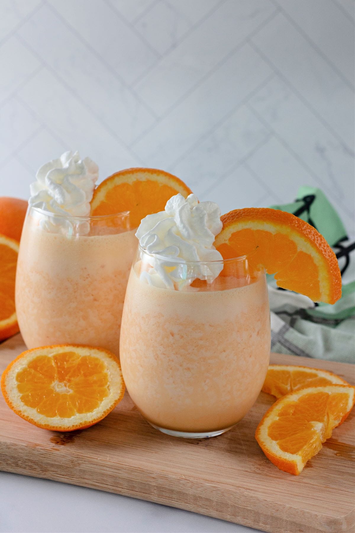 two glasses of orange julius with whipped cream and orange slices