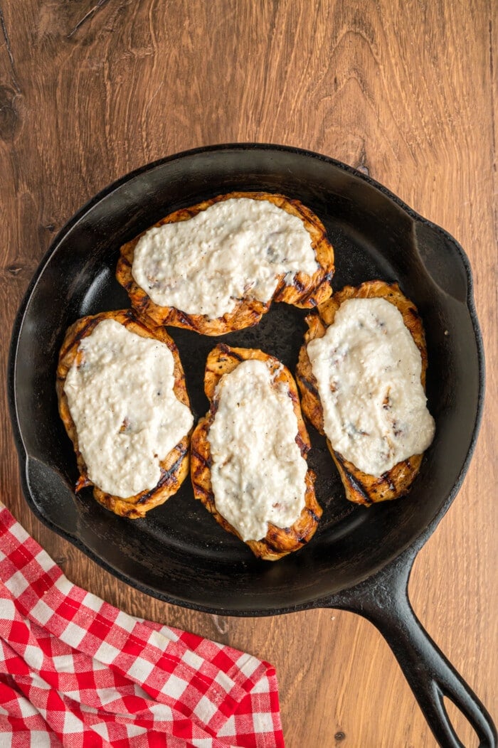 Grilled chicken breasts topped with ranch spread in a cast iron skillet
