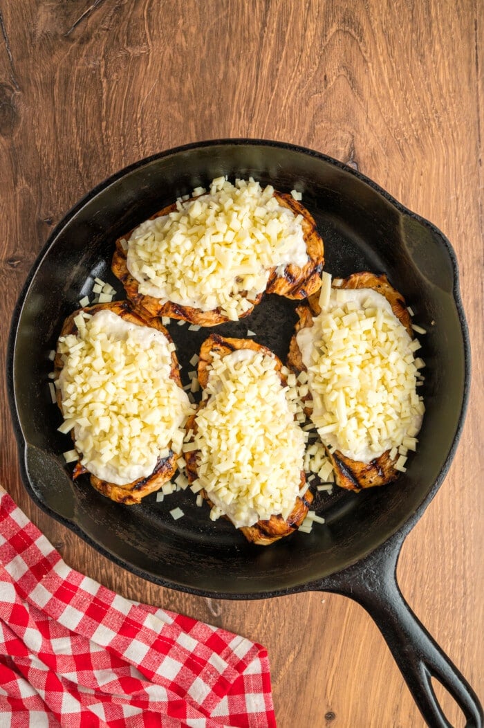 Grilled chicken breasts topped with parmesan cheese and ranch spread in a cast iron skillet