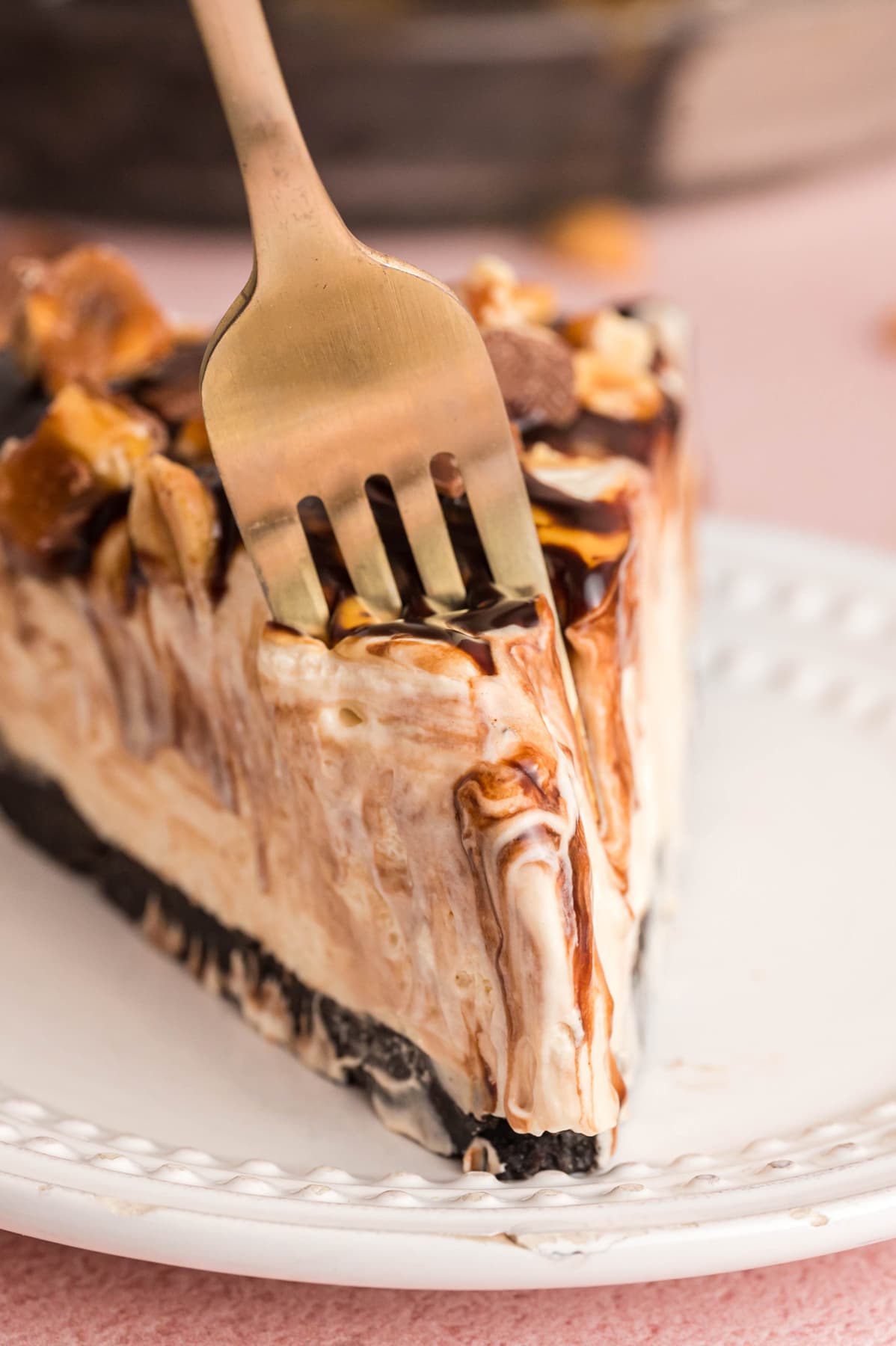 A slice of Snickers Pie on a white plate with a fork taking a bite.