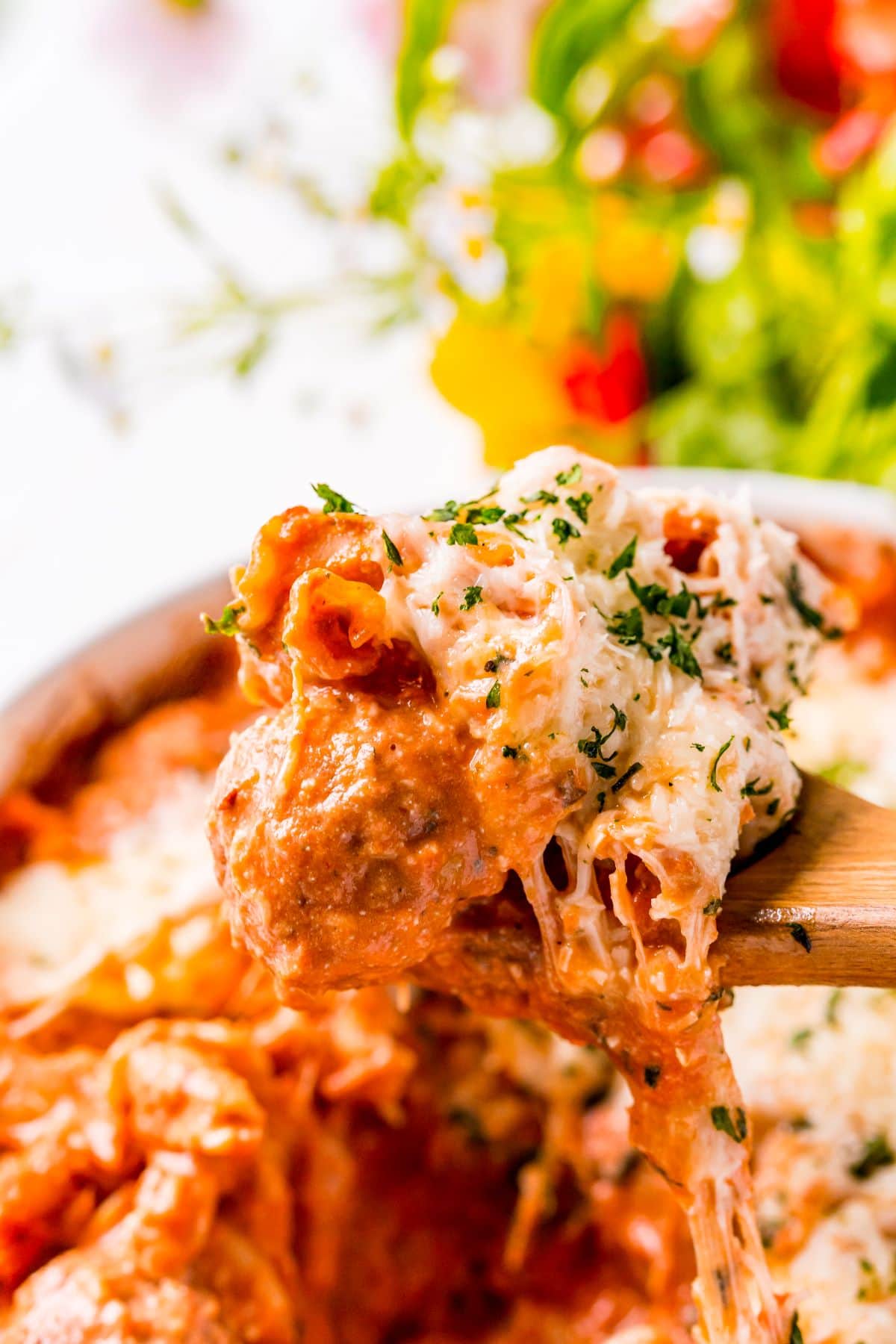 a wooden spoon with meatball pasta bake on top