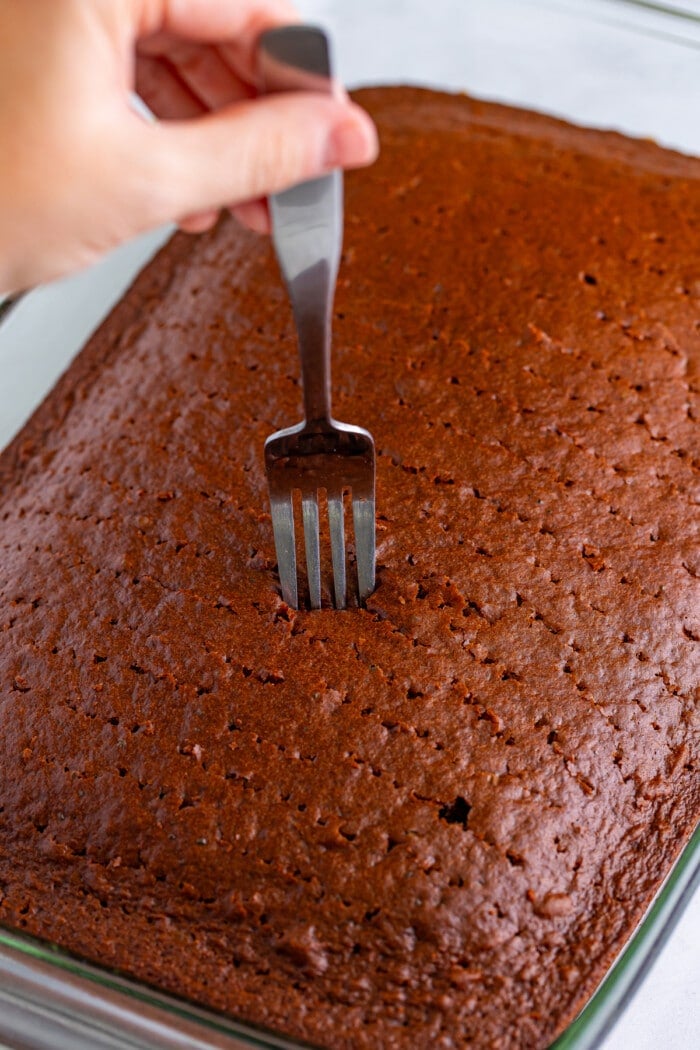 Poking holes in a chocolate cake with a fork.
