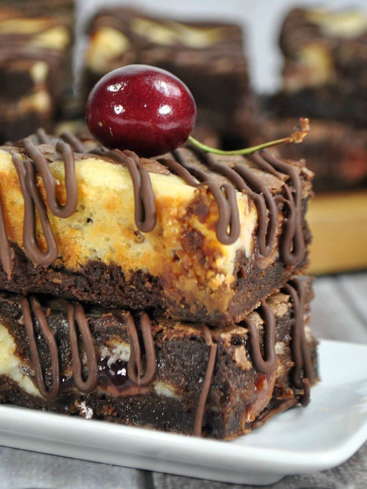 Cherry Pie Brownie Cheesecake Bars with a cherry on top on a plate