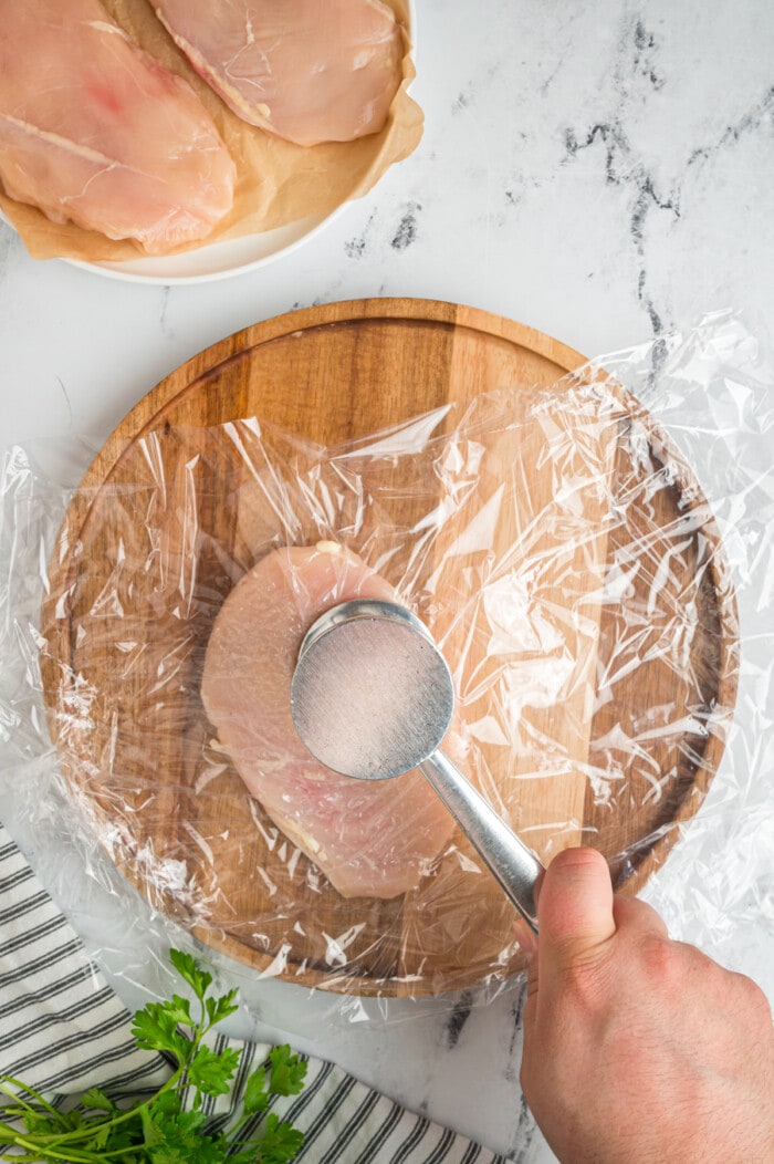 Chicken breast being pounded on a cutting board