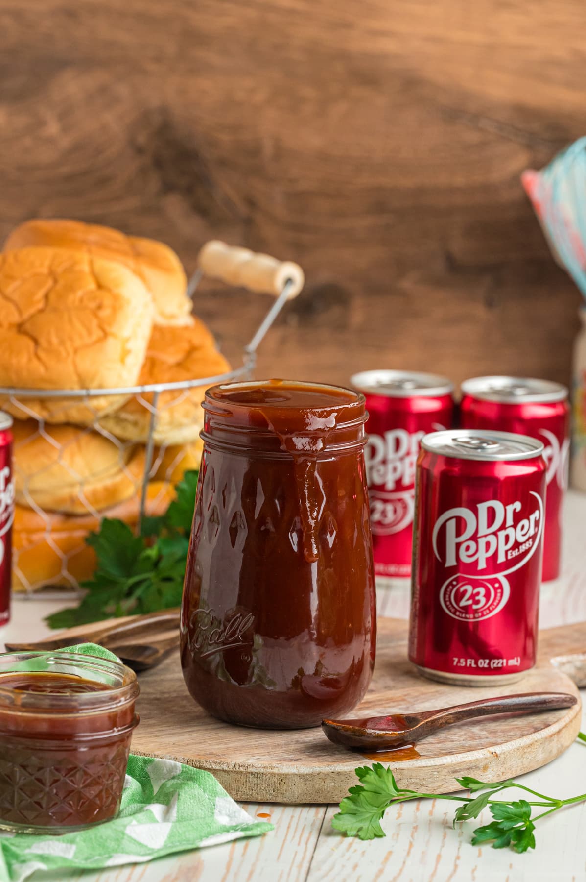 A jar of Dr Pepper BBQ sauce in front of cans of Dr Pepper and a bowl of buns