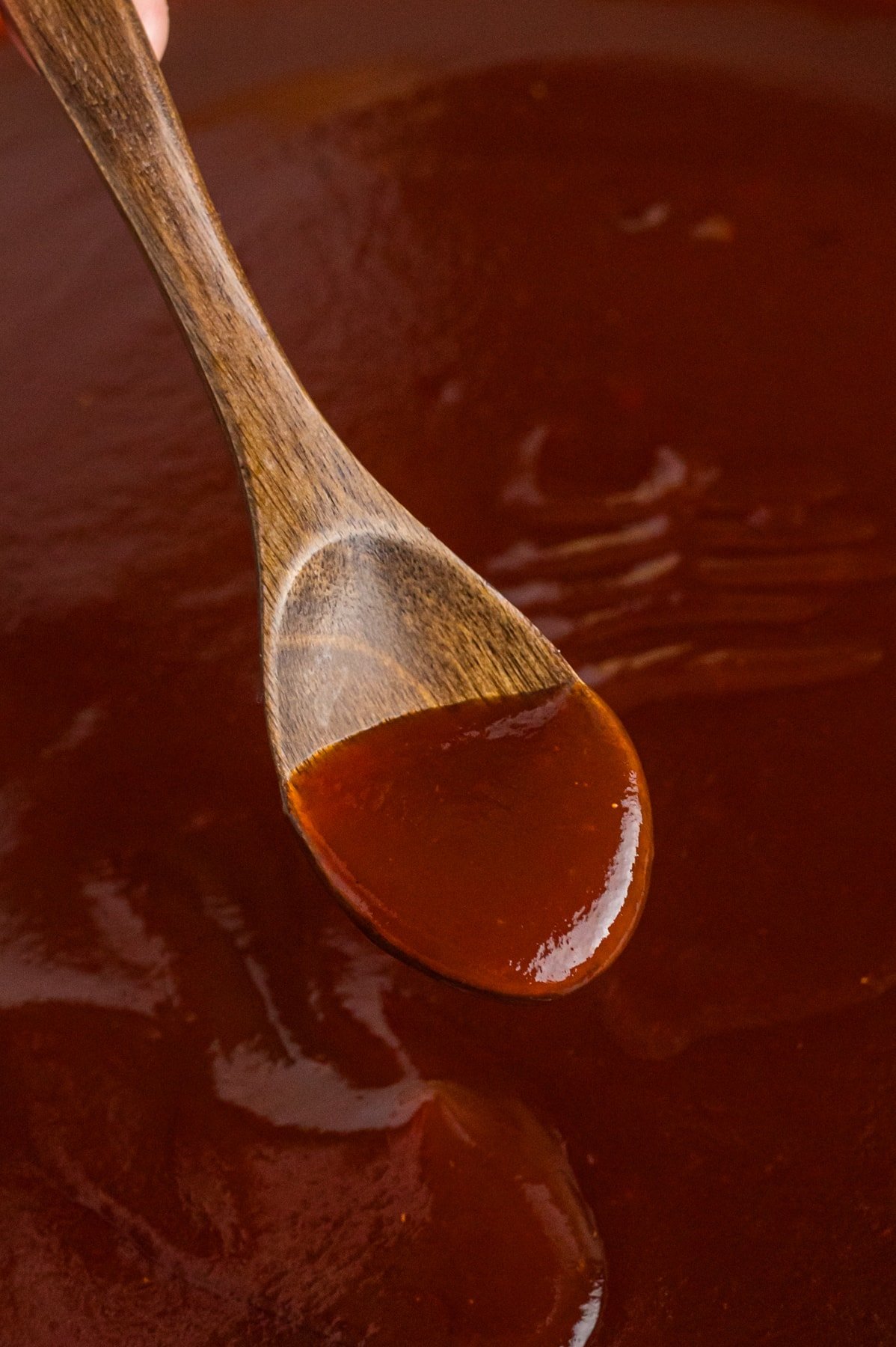 A wooden spoon stirring Dr Pepper BBQ sauce