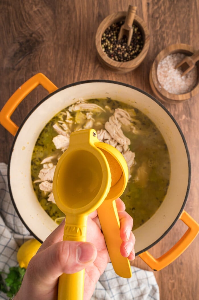 Lemon being squeezed into a pot of chicken orzo soup