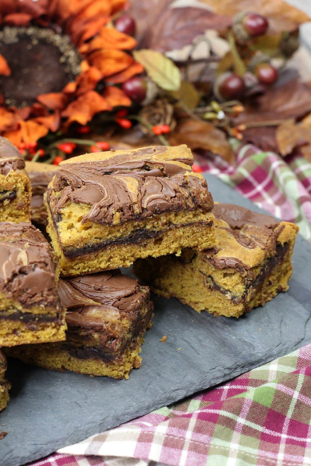 Chocolate Pumpkin Bars Recipe on a multi-colored cloth with Fall decorations behind it.