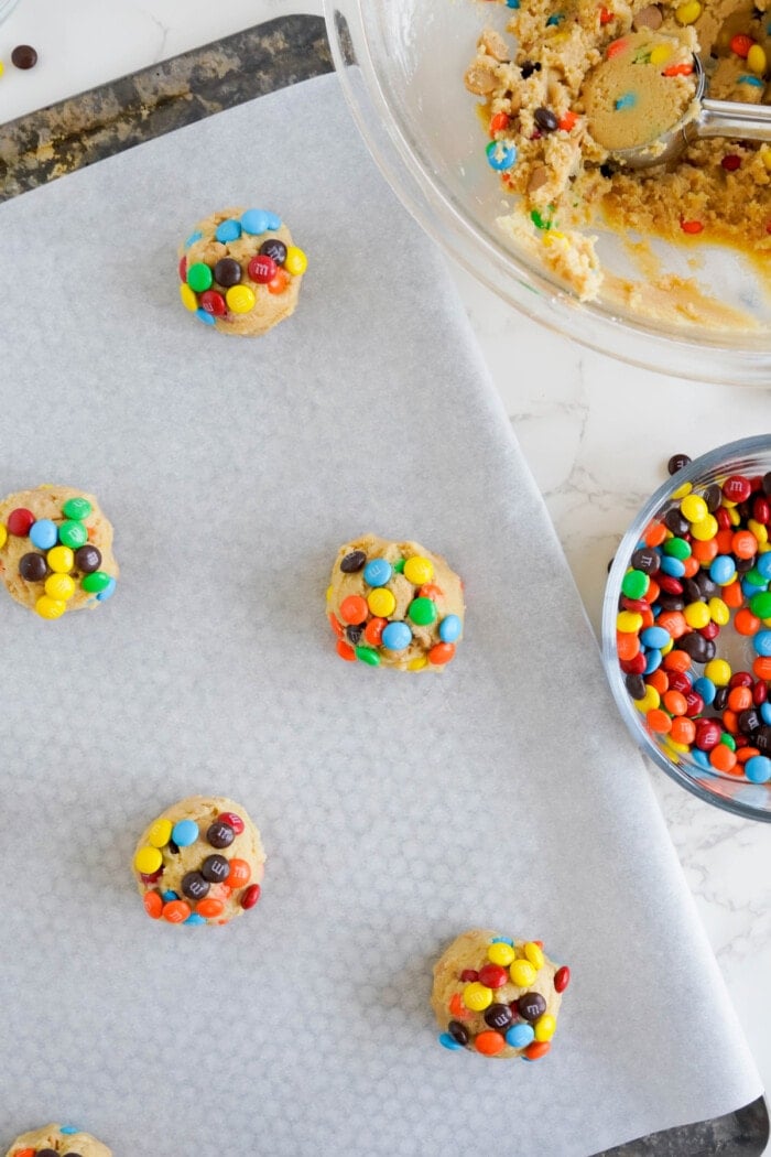 cookie dough balls rolled in M&M's on a baking sheet.