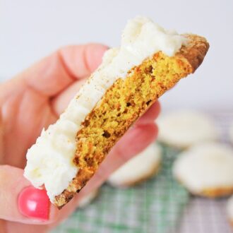 a carrot cake cookie with a bite taken out being held in someone's hand