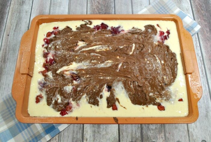 remaining brownie batter spread over cheesecake filling and cherries