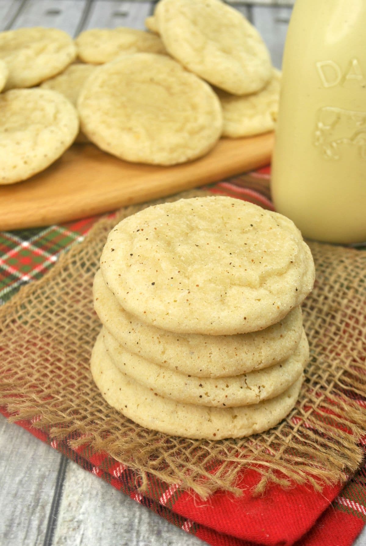 a stack of four eggnog cookies with a bottle of eggnog and eggnog cookies on a board