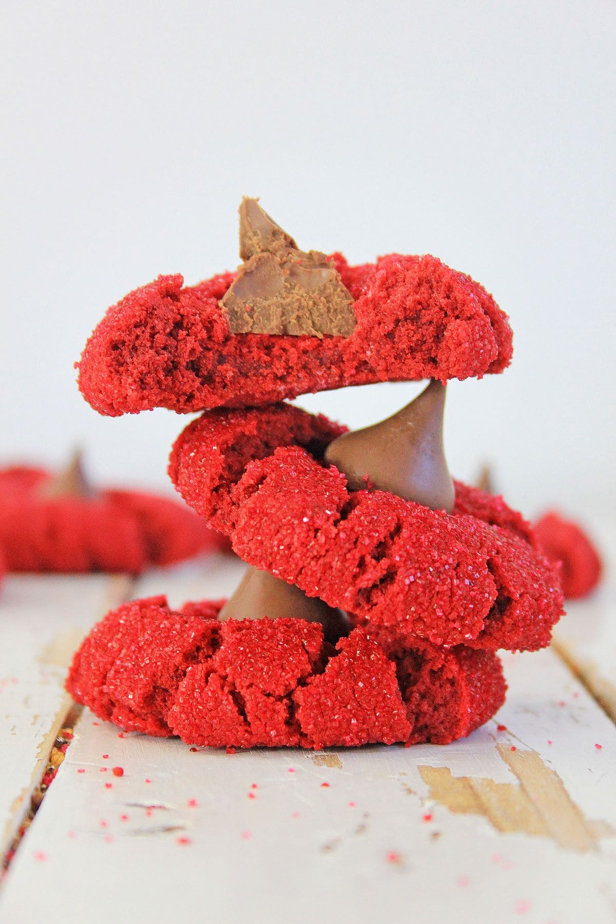 Three red velvet peanut butter blossoms stacked on a wooden countertop.