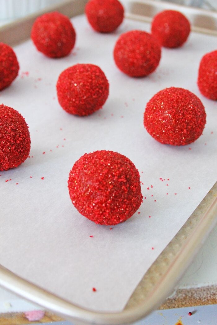Red velvet peanut butter cookie dough balls rolled in sugar, lined up in rows on a baking sheet.