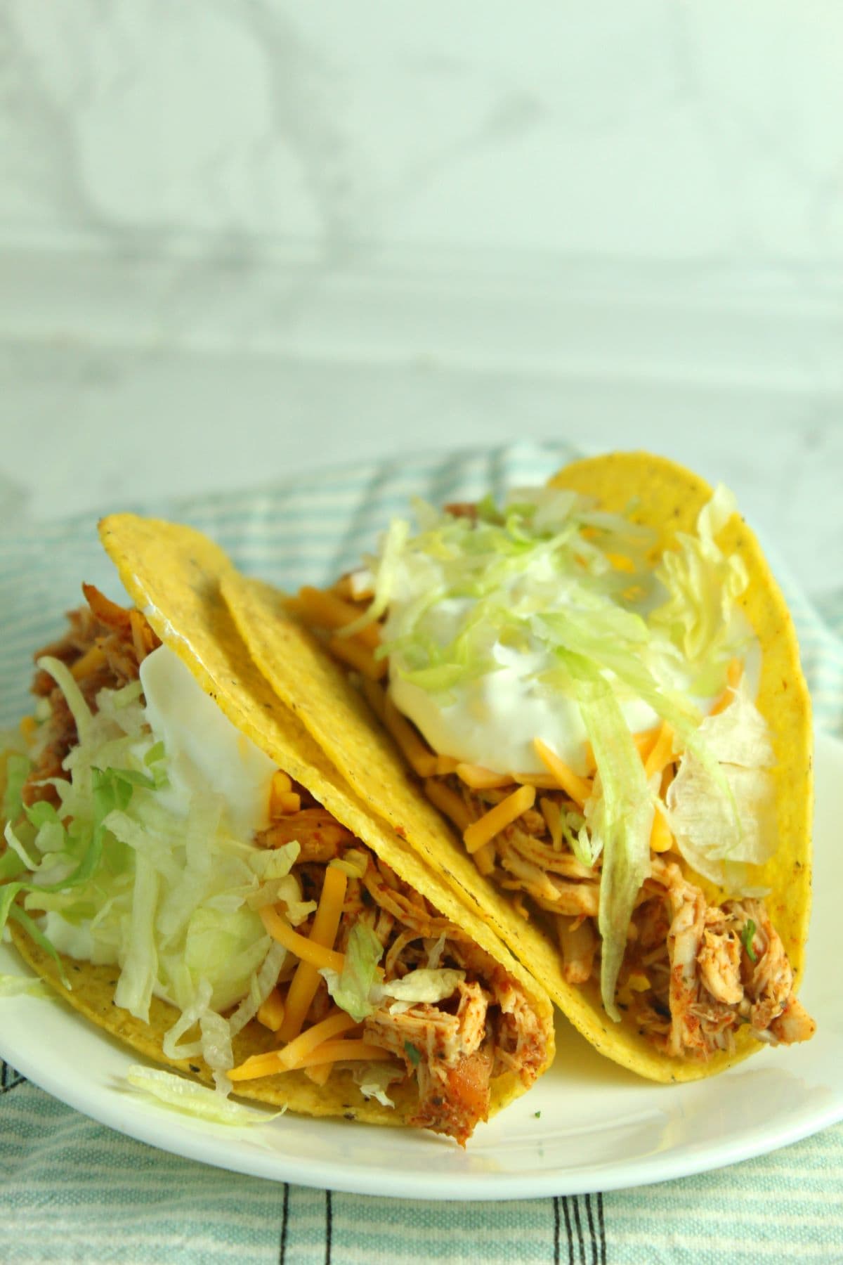 two chicken tacos with lettuce, sour cream and cheese on a white plate