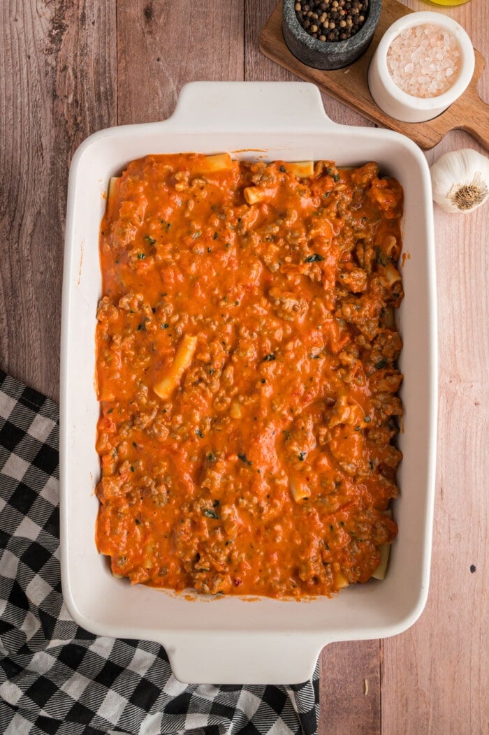 Ground sausage meat sauce poured over ziti noodles in a casserole dish.