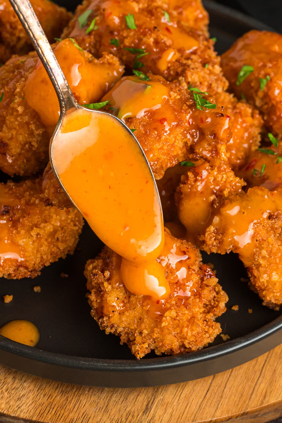 A spoon of bang bang sauce being drizzled over chicken