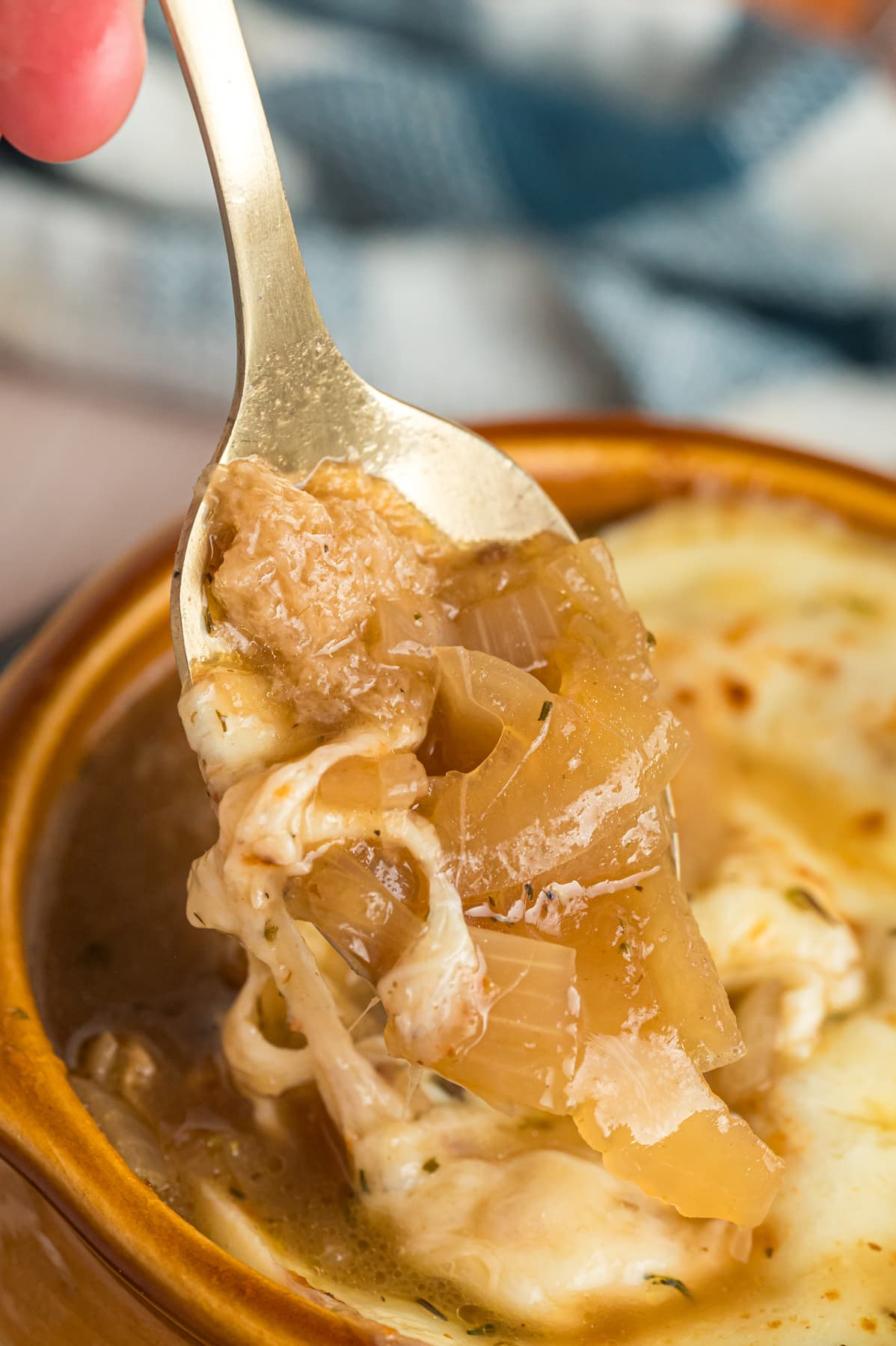 A spoon in a bowl of French onion soup showing the caramelized onions