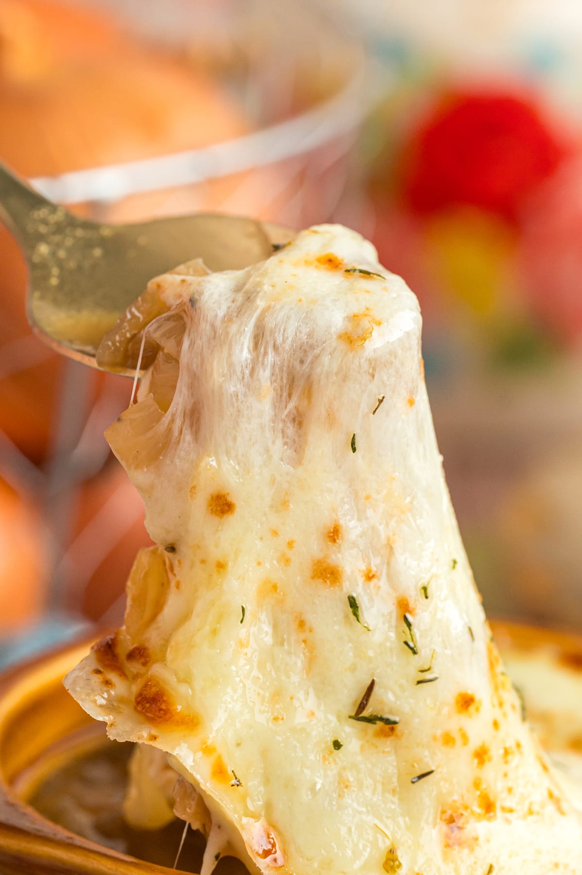 A close up of the cheese being pulled up from a bowl of French onion soup