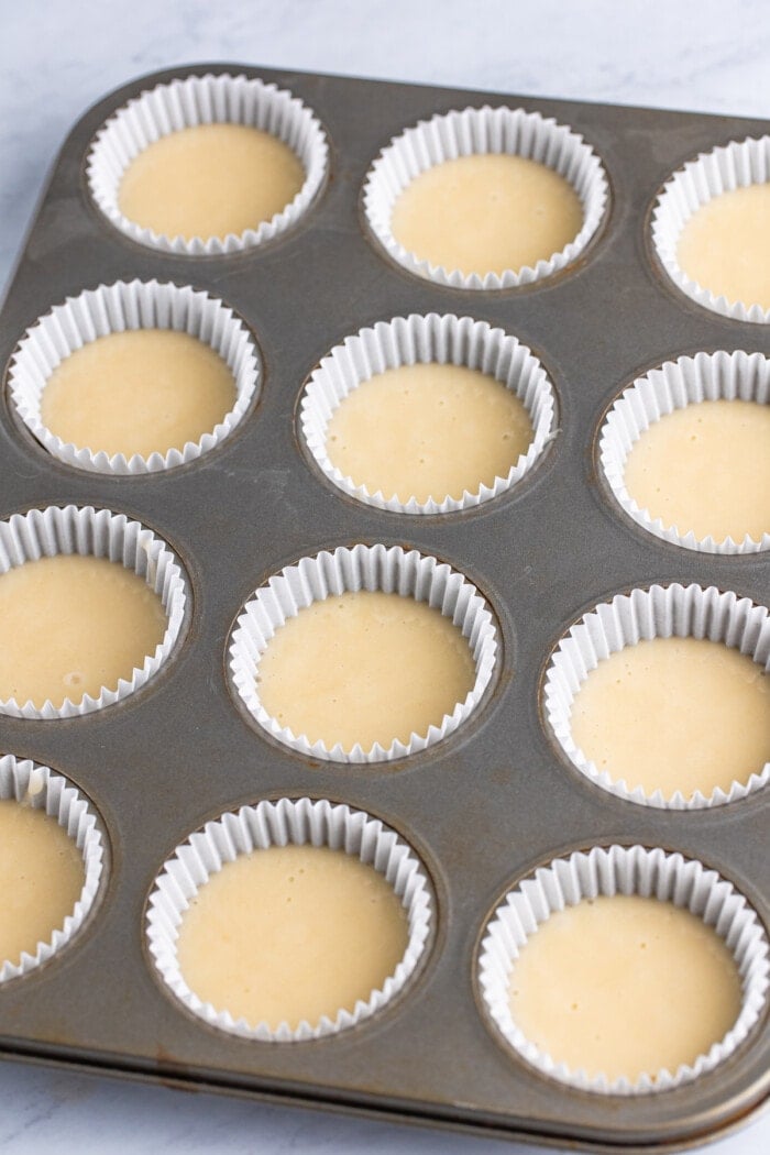 Cupcake batter in white liners in a cupcake baking pan.