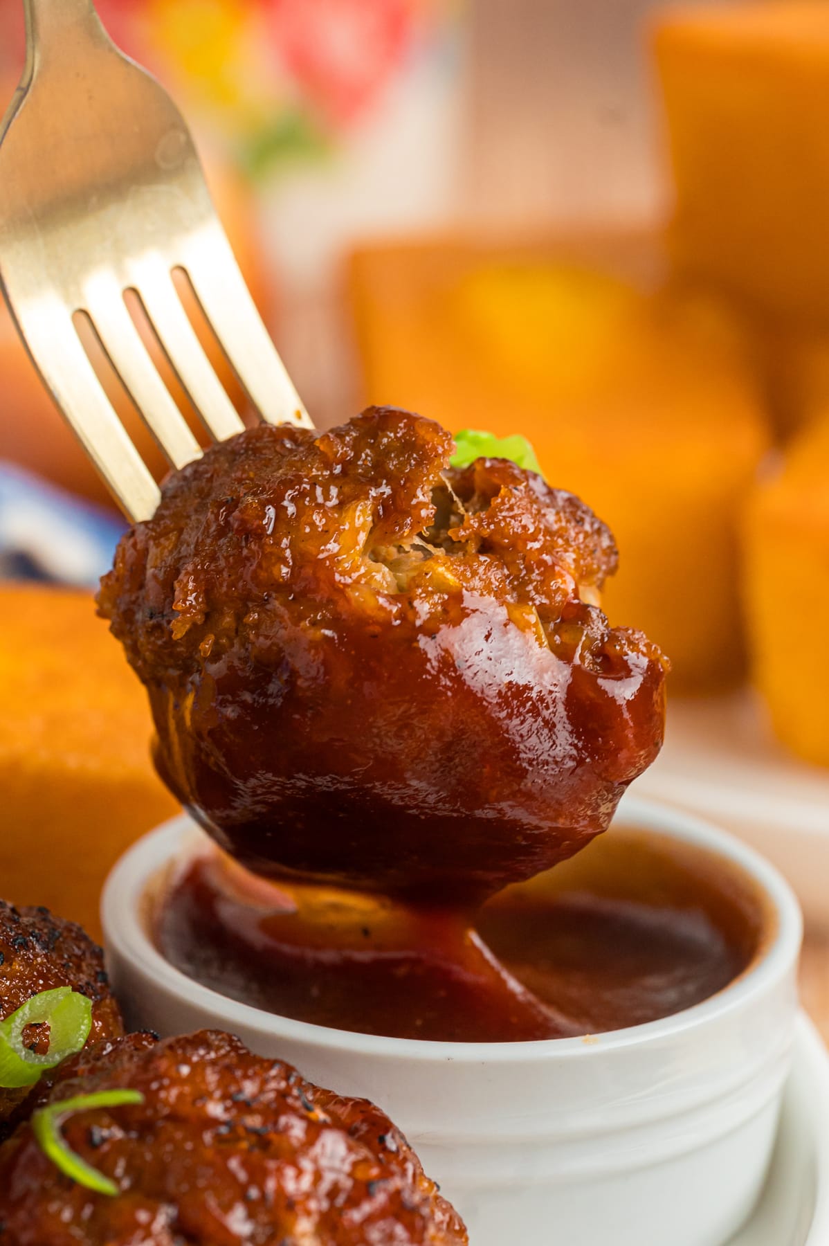 A meatball on a fork dipped in BBQ sauce