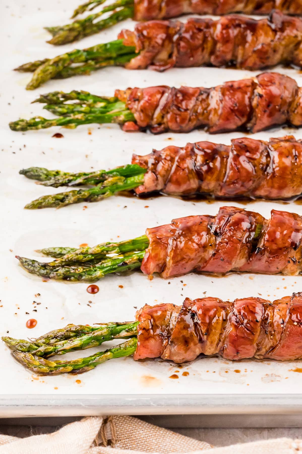 Close up of bundles of asparagus wrapped in bacon on a baking sheet