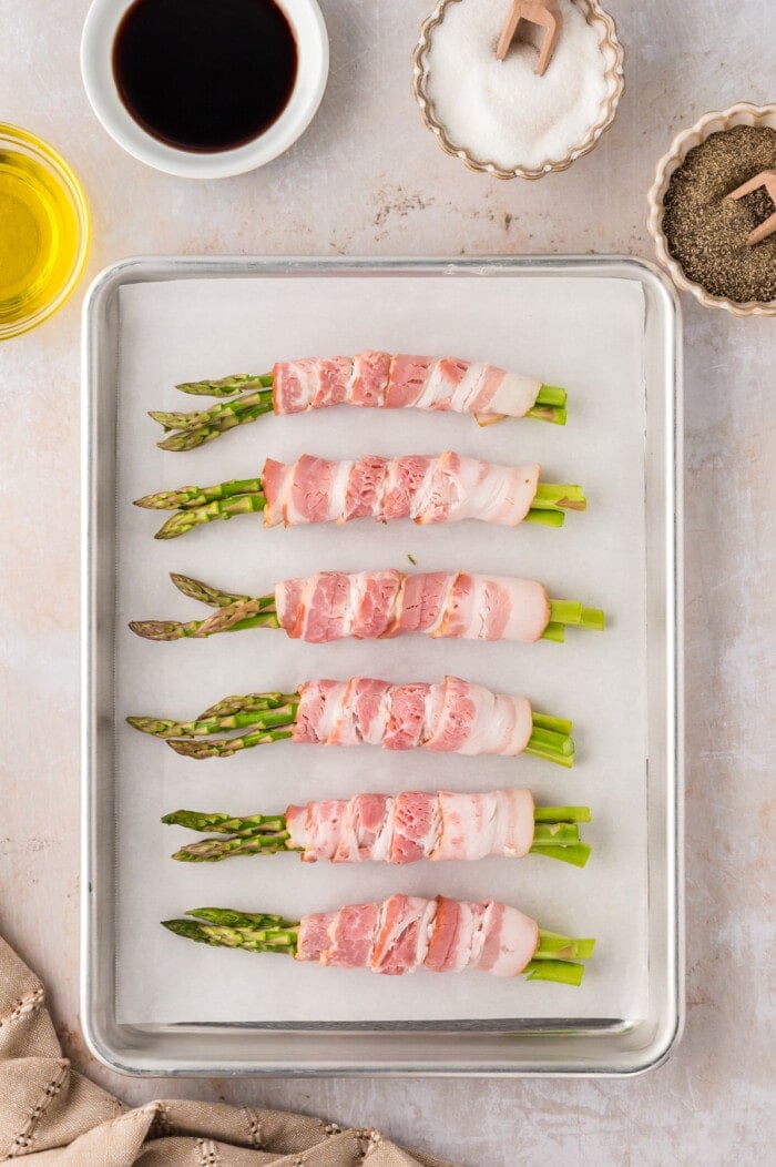 Bundles of asparagus wrapped in bacon on a baking sheet