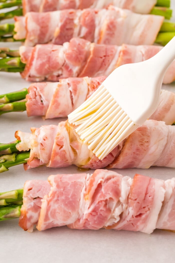 Oil being brushed on bacon wrapped asparagus