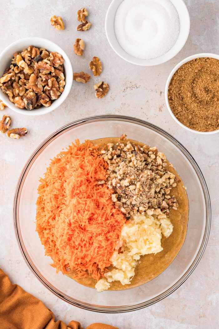 Shredded carrots, pecans, and pineapple added to carrot cake batter in a bowl