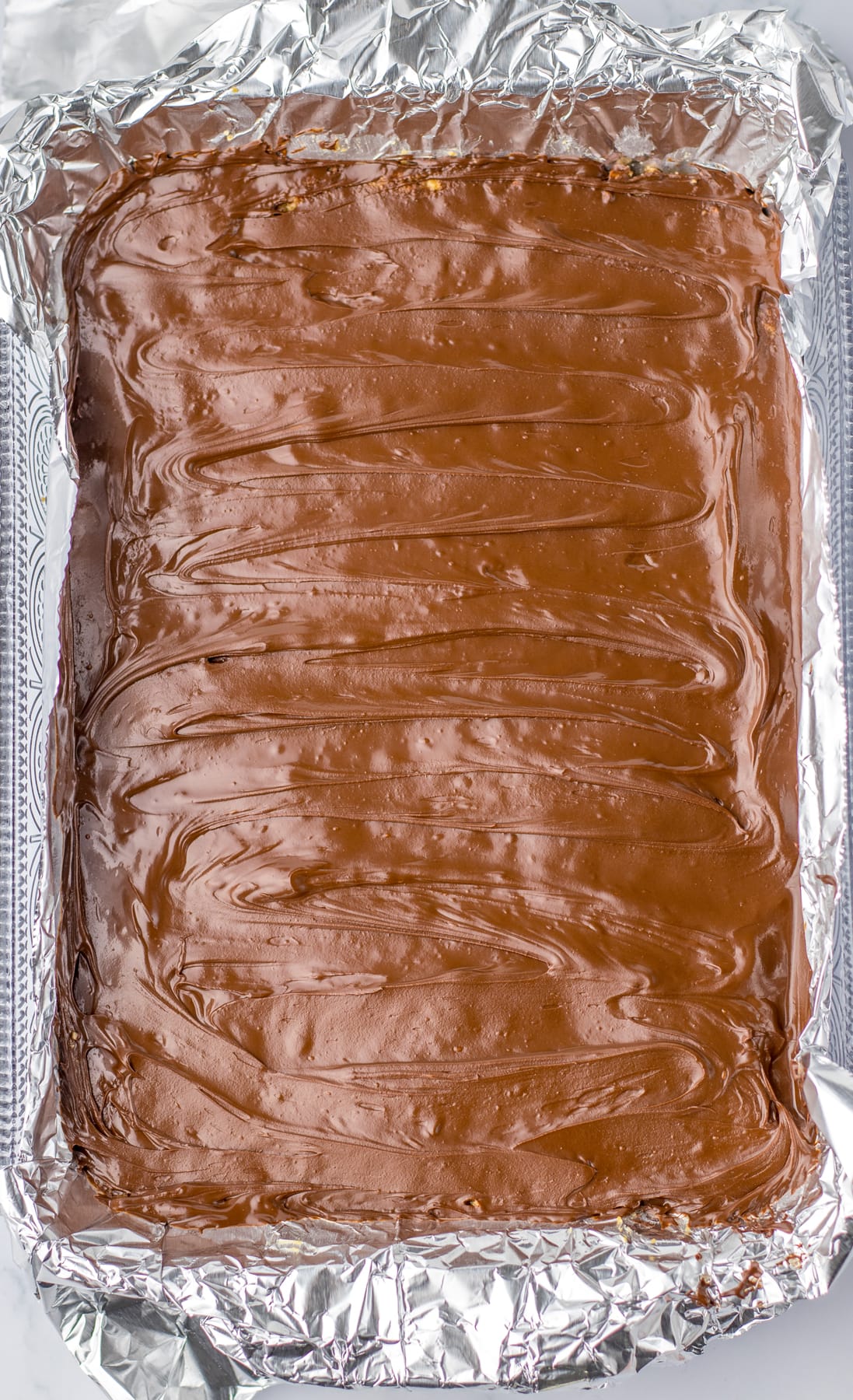 melted chocolate on top of crust for Peanut Butter Pretzel Bars