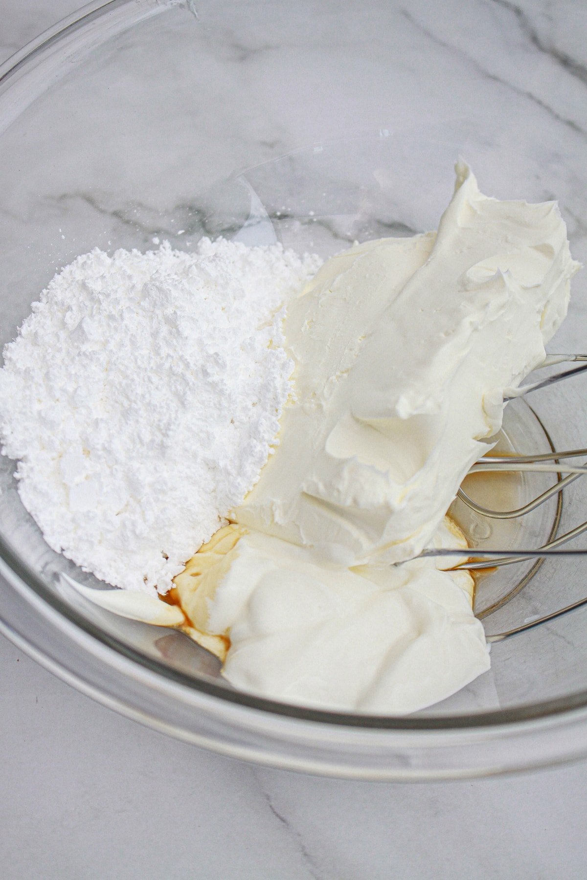 Cream cheese, powdered sugar, vanilla, and sour cream in a glass mixing bowl