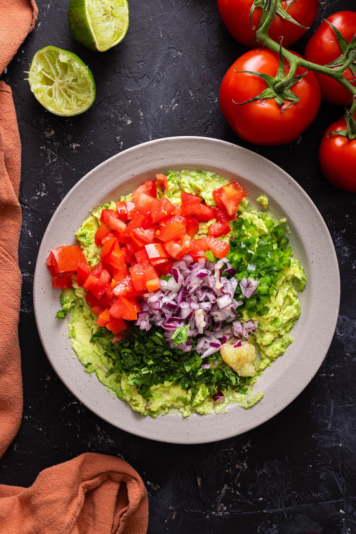 Diced tomatoes, red onions, cilantro, jalapenos, and garlic with smashed avocados in a bowl.