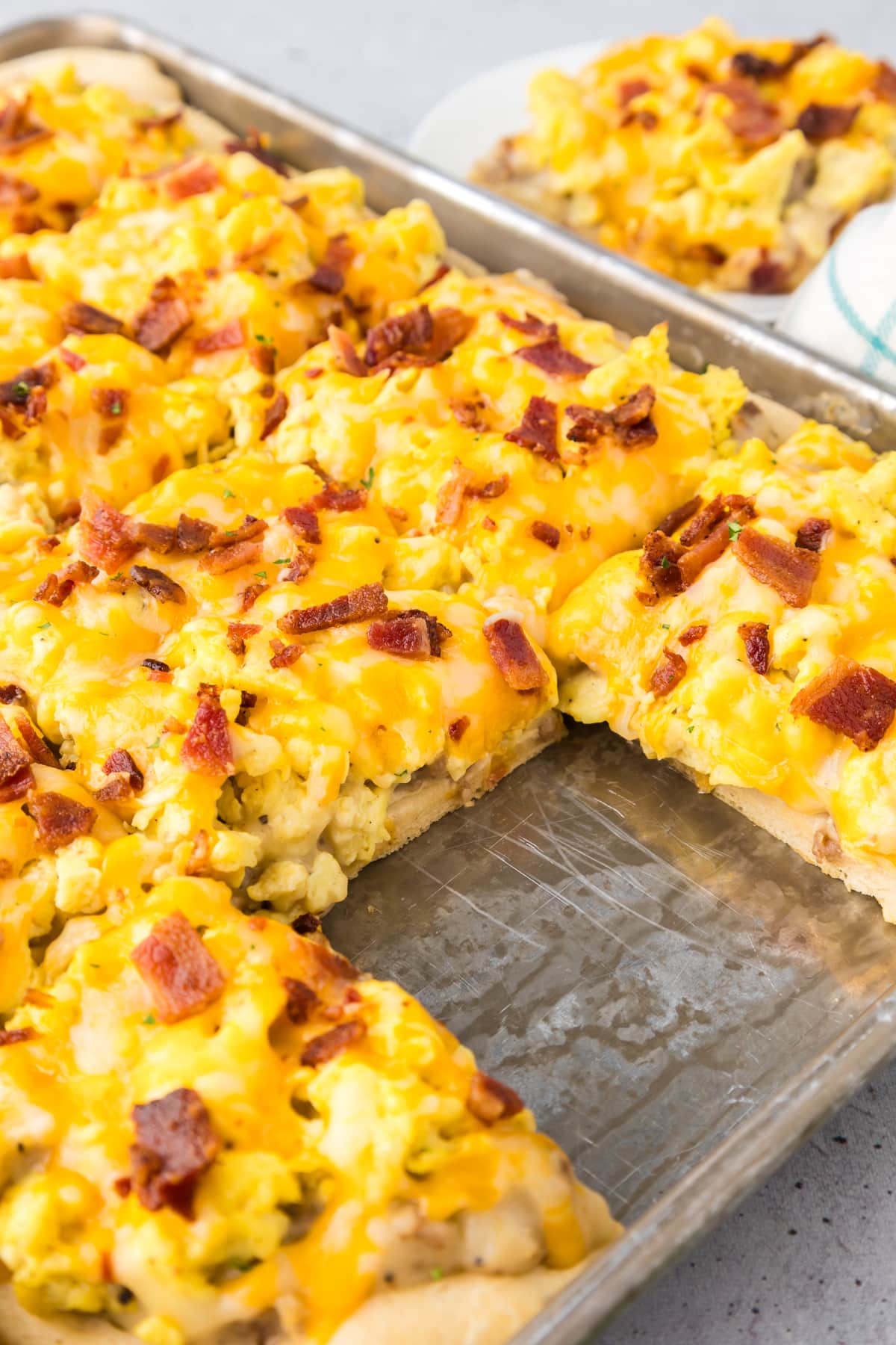 Breakfast pizza cut into square servings in a baking sheet.