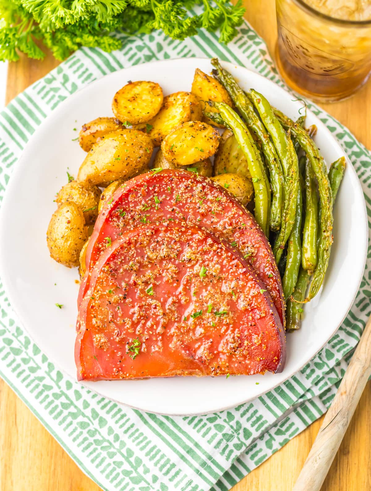 Ham steak with roasted potatoes and green beans on a white plate.