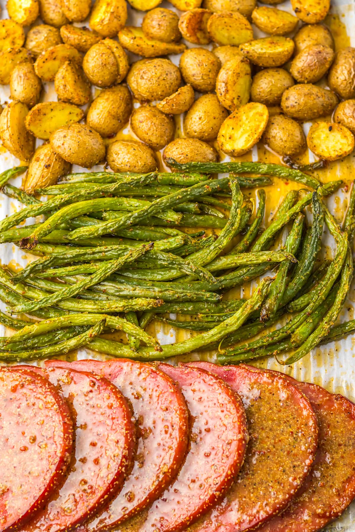 Ham steak with roasted potatoes and green beans on a parchment-lined baking sheet.
