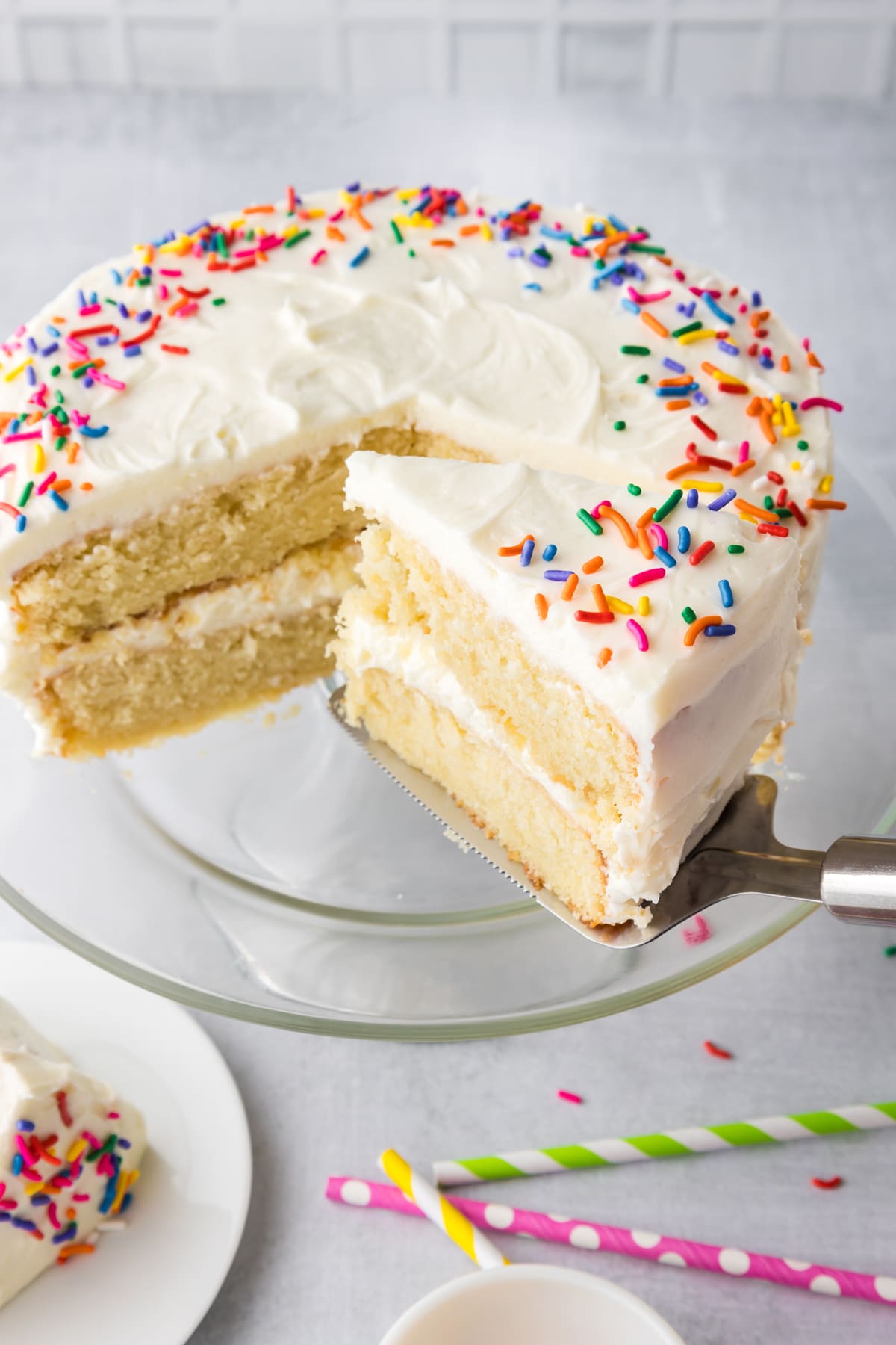 Overhead view of a vanilla layer cake with a slice being served