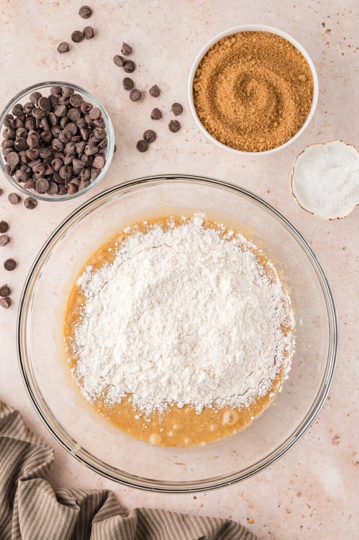 Flour added to wet cookie dough ingredients in a bowl.