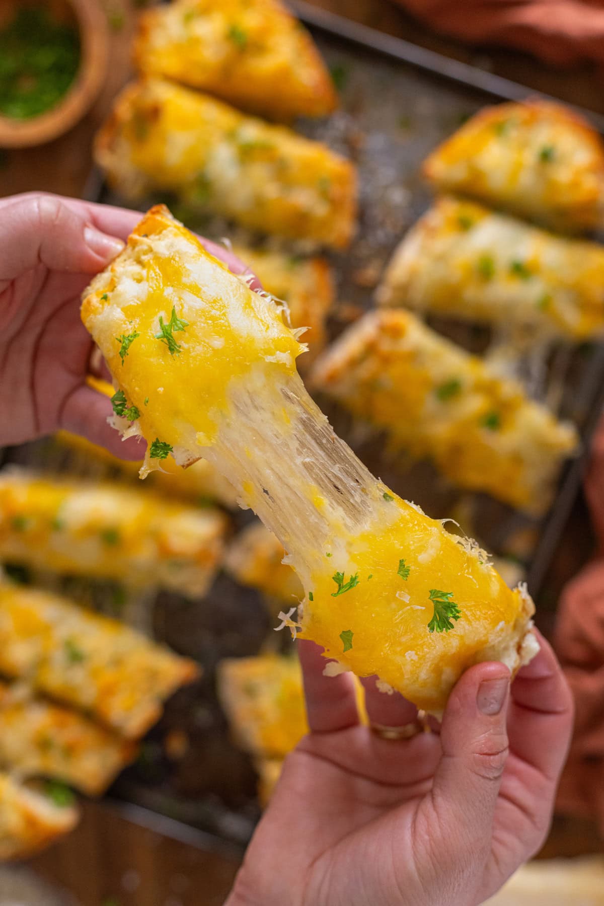 A hand pulling a cheesy garlic breadstick in half to show the cheese