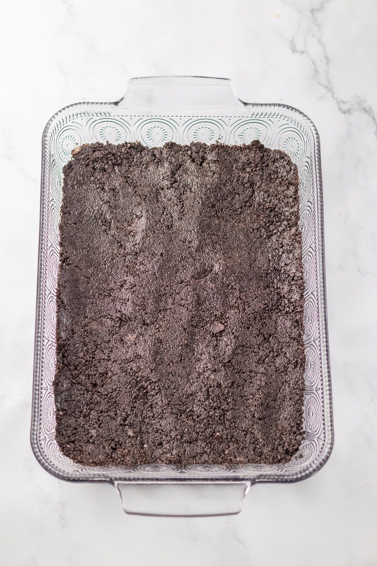 Crushed Oreos layered in the bottom of a glass 13 x 9 inch baking dish.