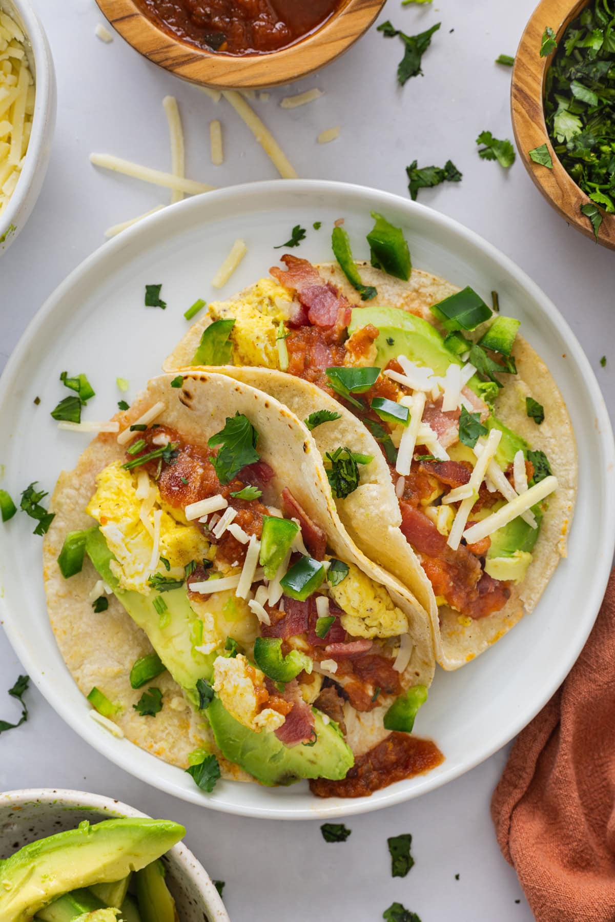 These homemade Breakfast Tacos are savory, cheesy, and everything you could want in a corn tortilla! Serve them for any meal or meal prep so you can enjoy them all week. Two breakfast tacos on a white plate.