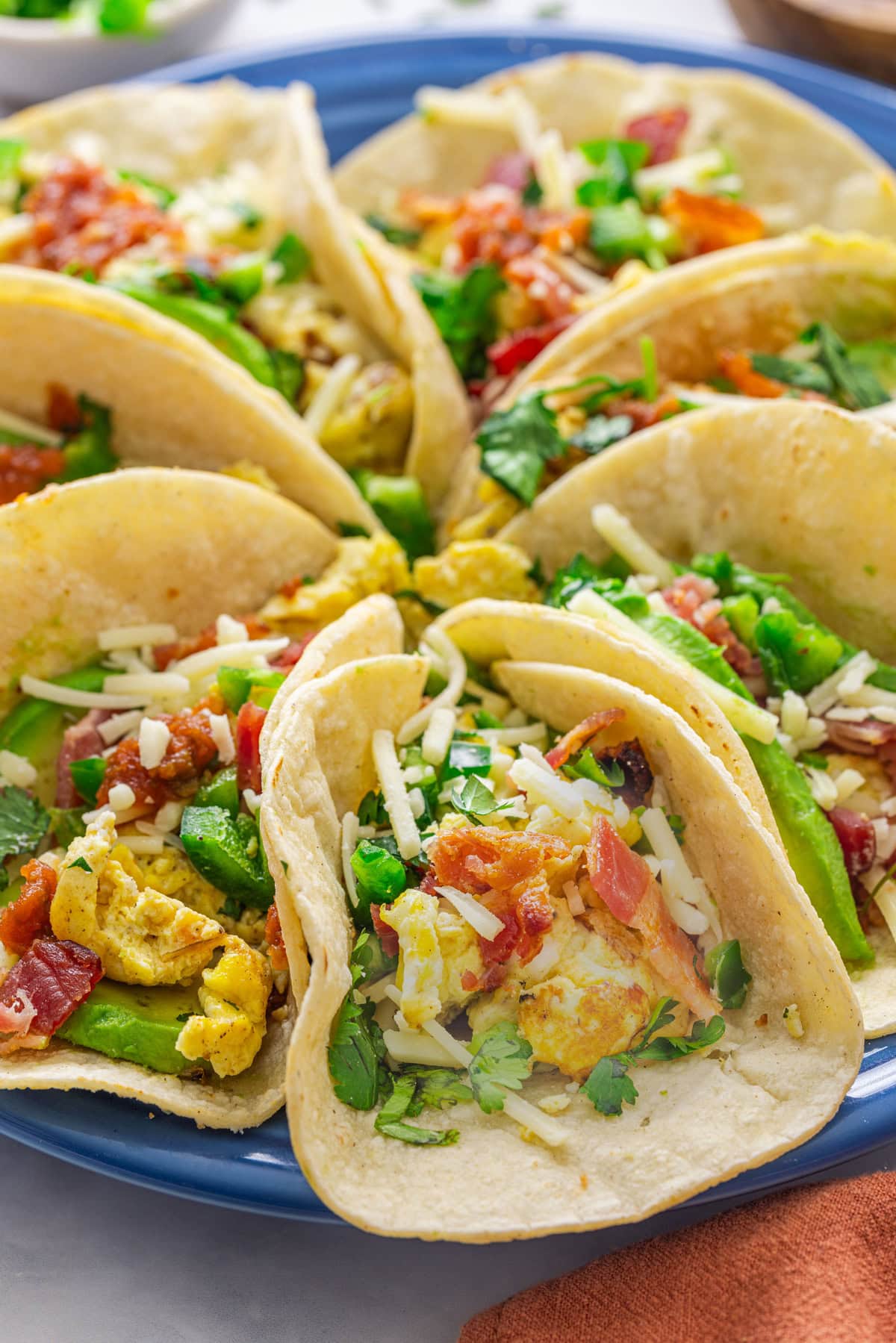 These homemade Breakfast Tacos are savory, cheesy, and everything you could want in a corn tortilla! Serve them for any meal or meal prep so you can enjoy them all week. Breakfast tacos on a blue plate.