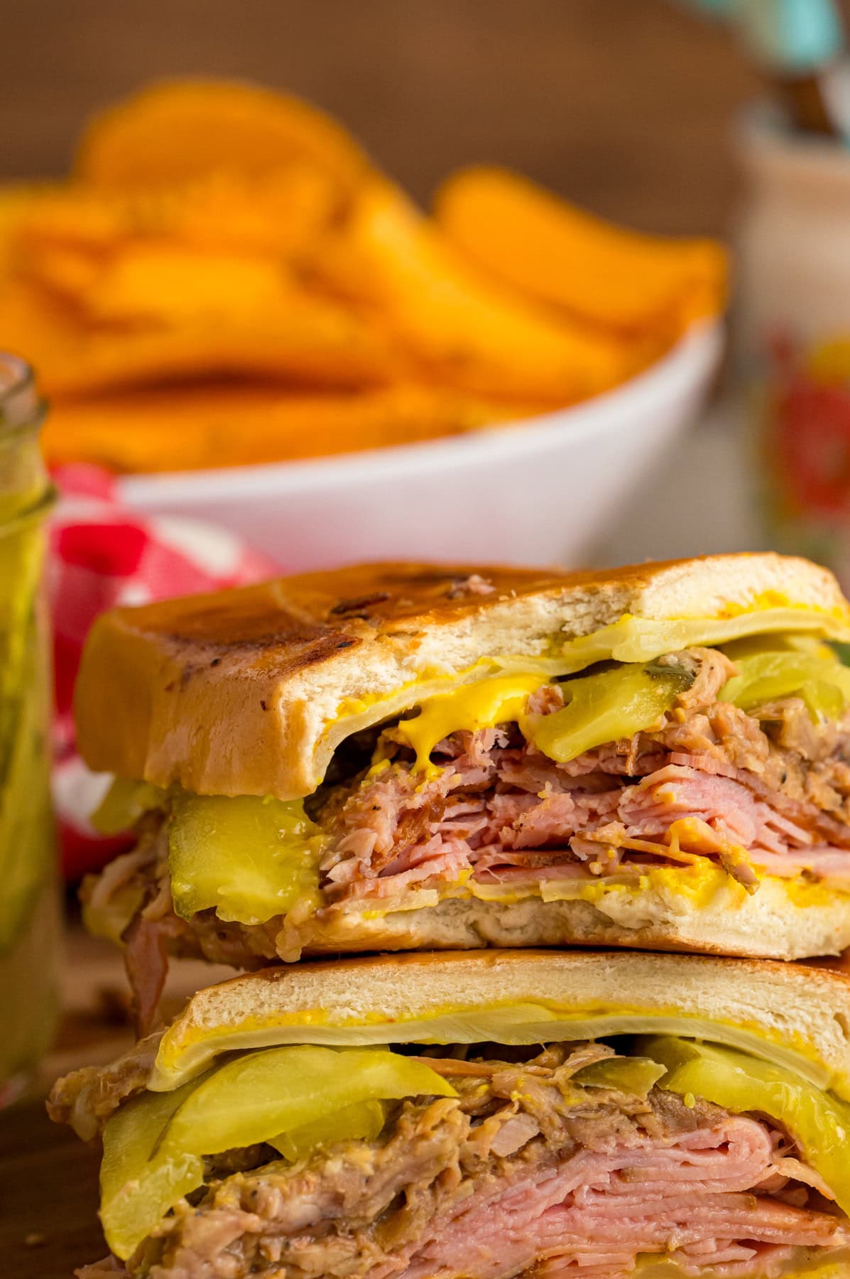 Two halves of a Cuban sandwich with a bite missing to show the ingredients inside