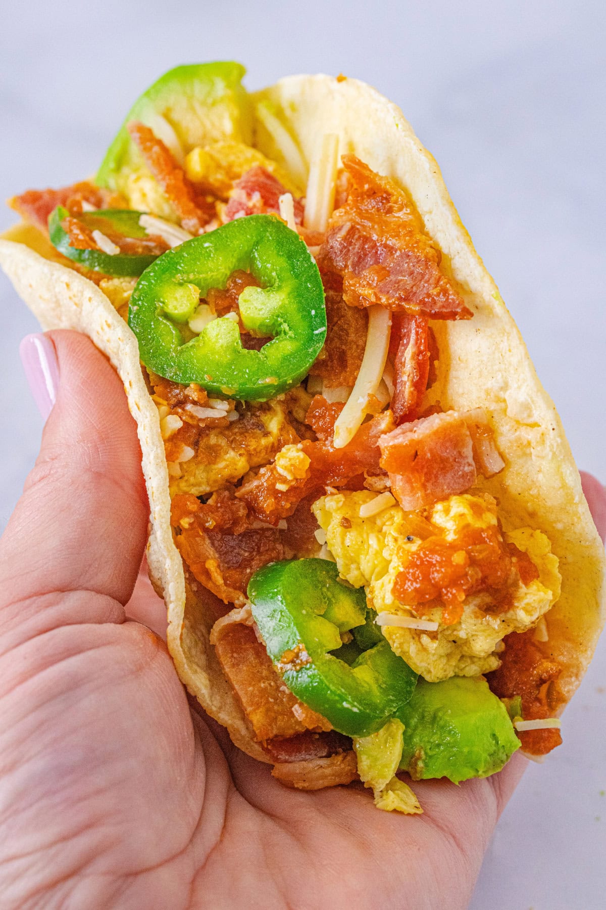 These homemade Breakfast Tacos are savory, cheesy, and everything you could want in a corn tortilla! Serve them for any meal or meal prep so you can enjoy them all week. hand holding a breakfast taco
