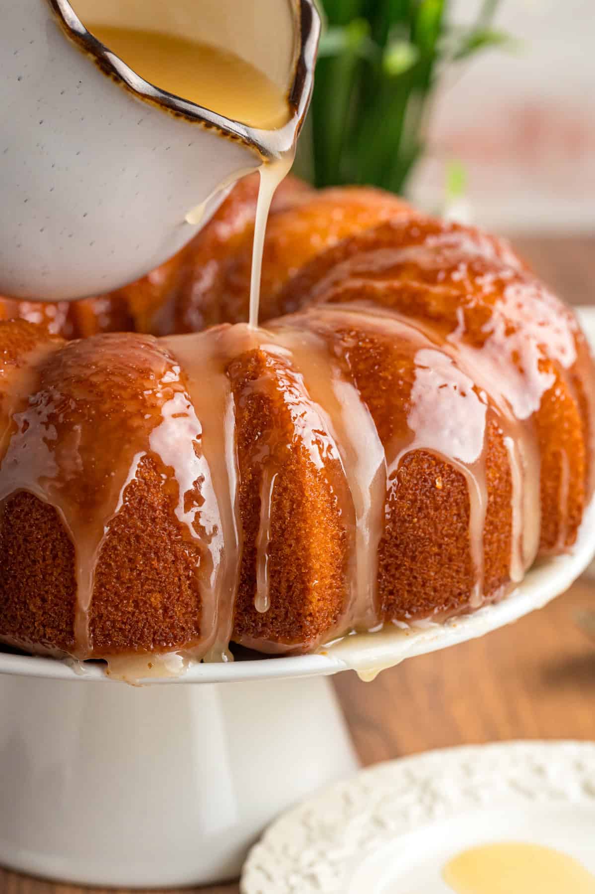 This Rum Cake recipe is made with spiced rum in the batter and a dark rum butter sauce drizzled on top. It's rich, moist, and easy! Butter rum sauce being poured over a rum bundt cake