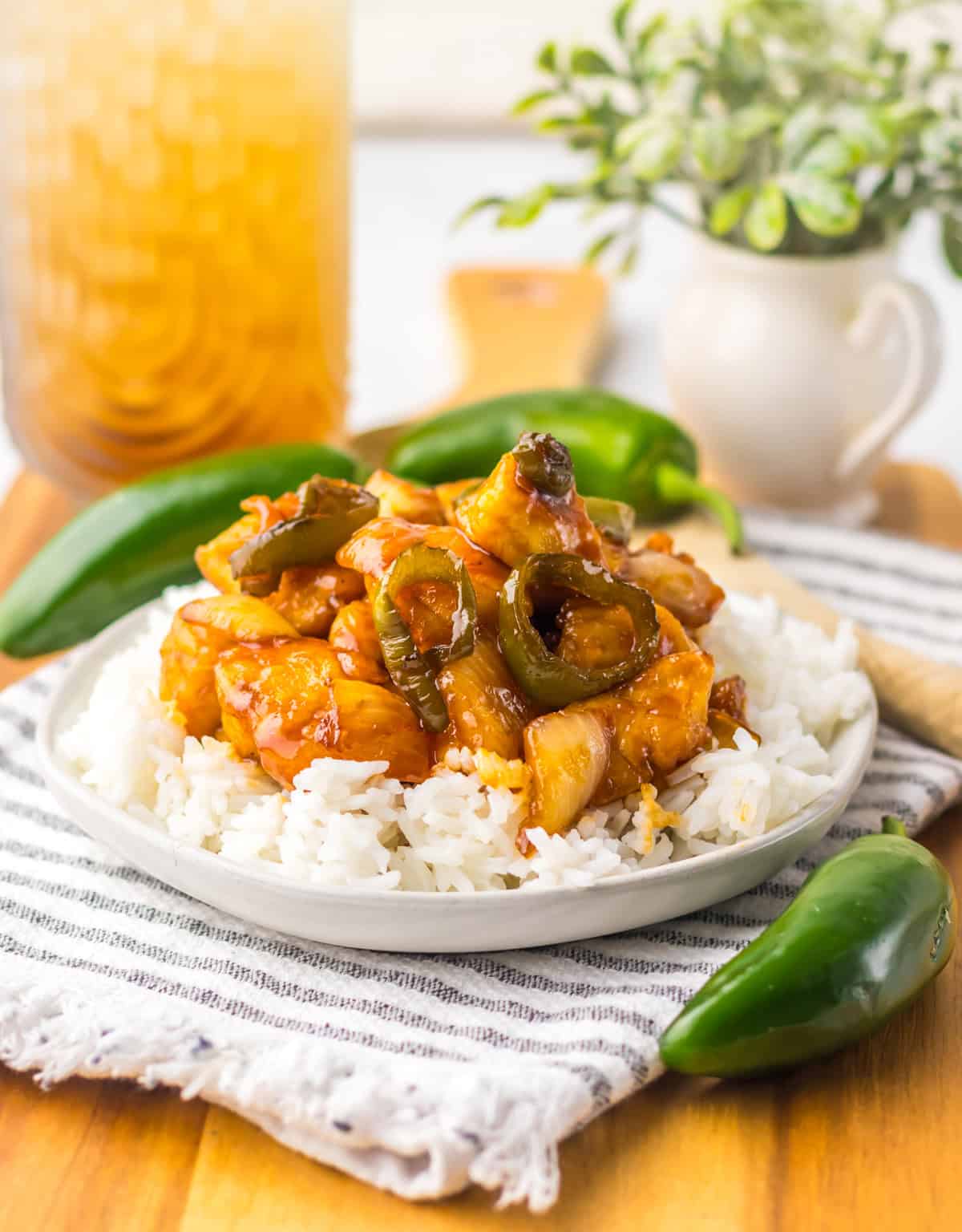 A wider view of jalapeño chicken plated on rice with jalapeño peppers placed around the dish and an iced drink in the background.