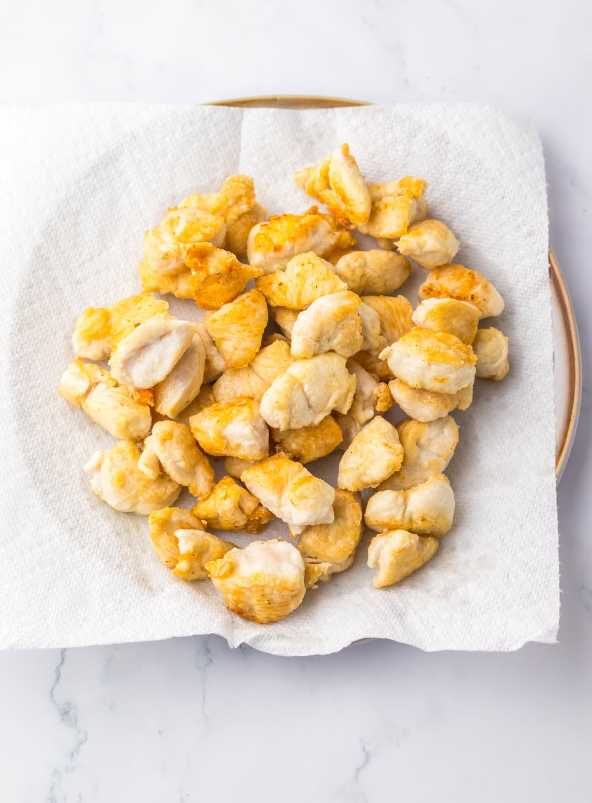 Lightly fried pieces of chicken resting on a paper towel to drain excess oil, as part of the preparation for jalapeño chicken.