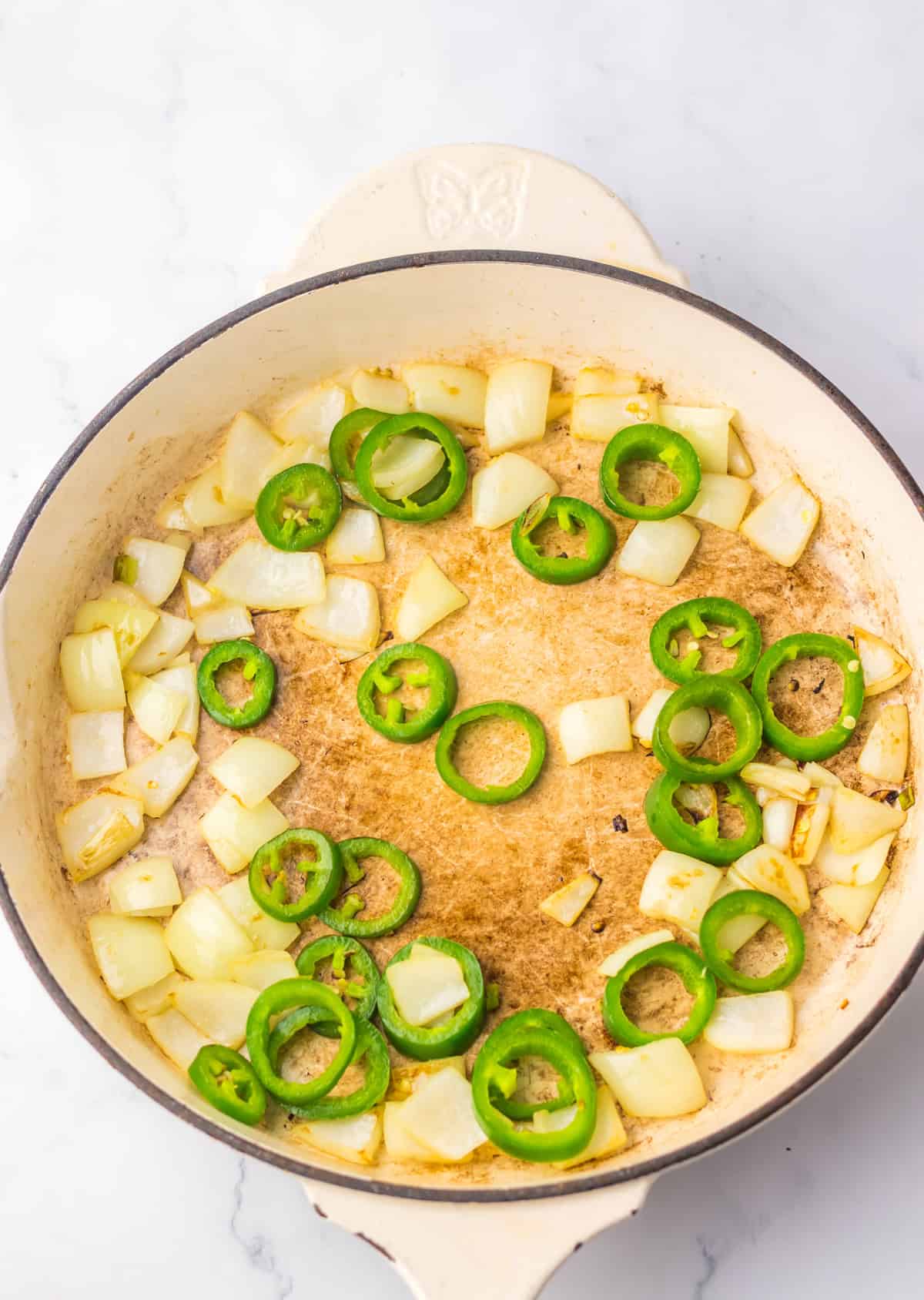 A close-up of onions and jalapeño slices being sautéed in a skillet as part of the jalapeño chicken preparation.