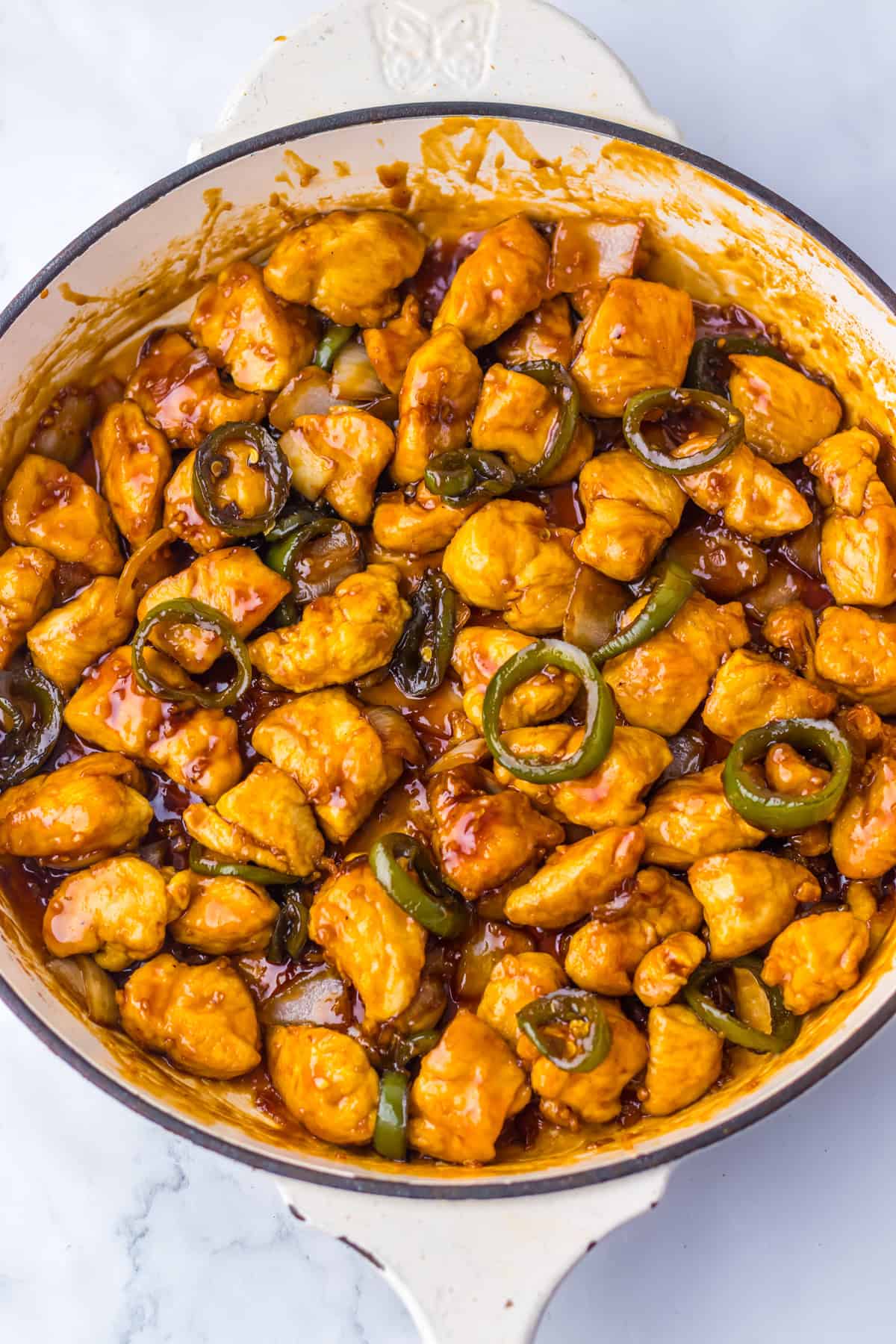 Jalapeño chicken simmering in a skillet, with pieces of chicken and jalapeño rings coated in a vibrant sauce.